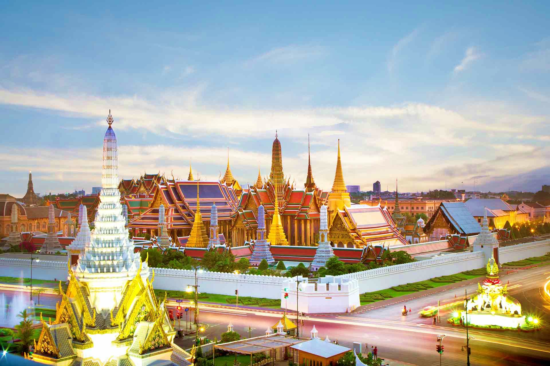 Grand Palace Bangkok at dusk with illuminated golden spires and traditional Thai temple architecture surrounded by white wall
